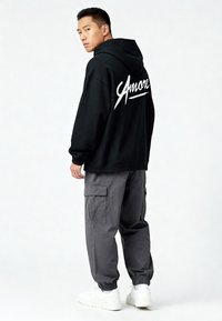 Felpa nera con grande testo bianco "Amore" sulla schiena, abbinata a pantaloni cargo grigi e sneakers bianche, con polsini elastici.