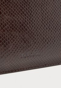 Superficie in pelle texturizzata marrone scuro con una stampa a diamante in rilievo e un sottile marchio "MAX&Co" in rilievo vicino al bordo inferiore.