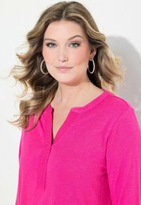Maglietta lunga a maniche rosa brillante con scollatura a V testurizzata e taglio morbido. Tessuto liscio con un leggero luccichio e dettagli a costine sul collo.