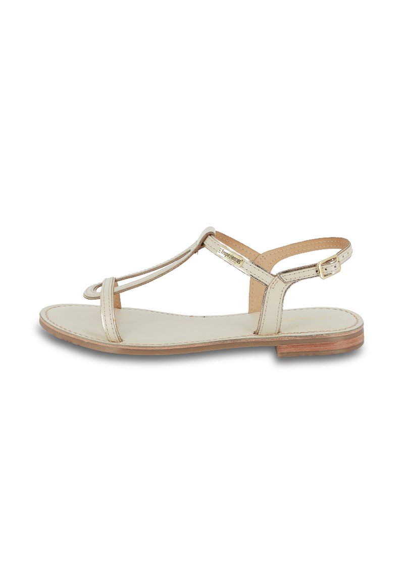 Sandalía plana beige con diseño de tira en T, correa de tobillo ajustable y parte superior de cuero suave con suela marrón clara.