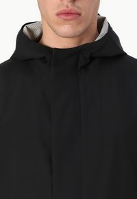 Zwarte hooded jacket met hoge kraag, minimalistisch ontwerp en gestreepte binnenvoering, die een gladde textuur en schone naden laat zien.
