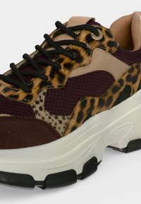 Chunky sneaker με μαύρα κορδόνια, βουργουνδί δίχτυ, μπεζ και καφέ πάνελ με ζωικό σχέδιο και παχύ λευκό πέλμα με μαύρες λεπτομέρειες.