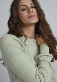 Lys grøn strikket sweater med ribbet rund hals og lange ærmer, der har en blød tekstur og en afslappet pasform.