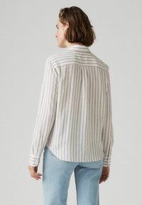 Lange mouwen gestreepte blouse van lichte stof met witte en paarse verticale strepen. Heeft een achterpand en knoopmanchetten, gecombineerd met jeans.