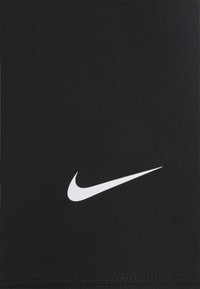 Hvid Nike swoosh logo på sort stof, der viser tekstur og syningsdetaljer i bunden.