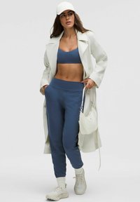 Sportovní outfit se světle šedým trenčkotem, tmavě modrou sportovní podprsenkou, odpovídajícími joggery, bílými teniskami a bílou kabelem.