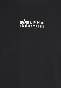 Černé tričko vyrobené z bavlny, s vyšitým bílým logem "ALPHA INDUSTRIES" a designovými prvky nad textem. Hladká textura.