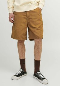 Pantaloni scurți de tip cargo maro, din bumbac, cu buzunare laterale, asortați cu adidași negri și șosete maro cu dungi. Croială casual, cu un design confortabil.