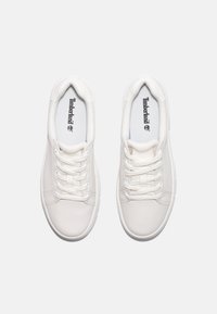 Hvite sneakers med en glatt overdel i lær og tekstil, flate hvite snørebånd og en logo trykt på innersålen. Rund tåform.