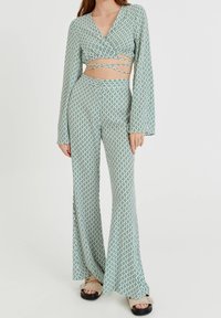 Tvådelad outfit bestående av en grön och vit mönstrad crop top med trumpetärmar och högmidjade utsvängda byxor. Texturerat tyg och korsningsdetaljer.