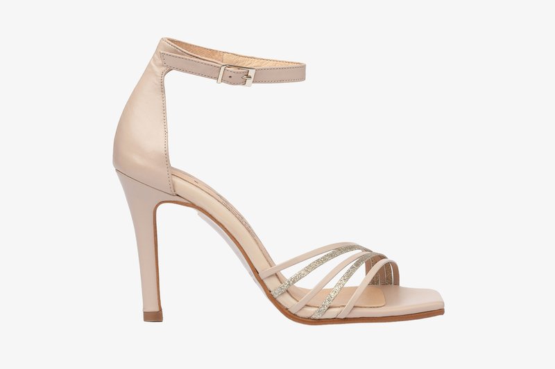Sándal de tacón alto beige con correa de cuero en el tobillo, punta abierta y múltiples tiras decorativas delgadas con acentos metálicos. Textura suave.