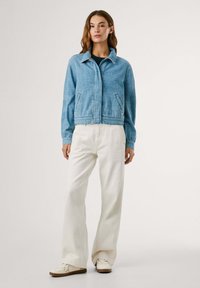 Light blue denim jacket with a cropped design, collar, and front pockets, paired with white wide-leg pants and beige sneakers.