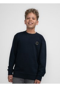 Marineblauwe sweatshirt met lange mouwen, ribbelmanchetten en -zoom, met een ronde patch op de linkerkant van de borst. Zachte stoftextuur.
