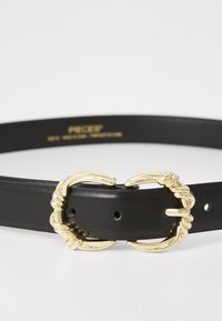 Ceinture en cuir noir avec une boucle en métal doré tordue. Comprend plusieurs trous d'ajustement le long de la sangle pour personnaliser la taille.