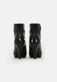 Stivali ankle neri con tacco realizzati in pelle liscia, dotati di punta arrotondata, chiusura con zip e fiocco decorativo con accenti dorati e perle.