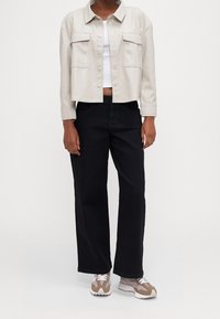 Kremowa kurtka z sztucznej skóry o kroju cropped z dwiema kieszeniami na piersi, w zestawie z czarnymi spodniami o szerokich nogawkach oraz beżowo-białymi sneakersami.