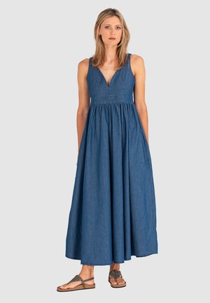 Denim maxi-jurk met een V-hals en zonder mouwen. Uitlopende silhouet, zijzakken en een lichte stof. Gemaakt in combinatie met platte sandalen.