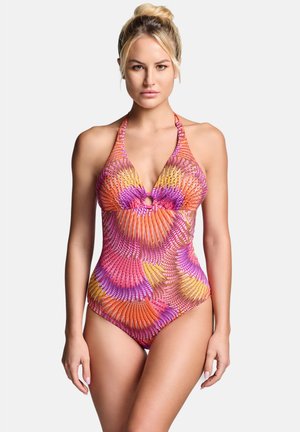 Blonde vrouw met haar in een knot draagt een halternek badpak met een oranje, roze en gele abstracte zwirlenpatroon op een witte achtergrond.