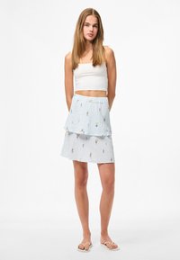 Vícevrstvová, světle modrá sukně s květinovou výšivkou, texturovaná tkanina, elastický pas. V kombinaci s bílým crop topem a světlými sandály.