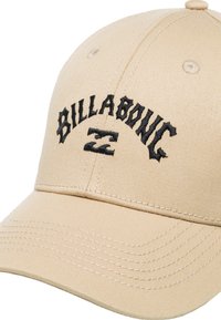 Beige kasket lavet af tekstureret stof, med sort broderet "BILLABONG" logo og syninger på skyggen.