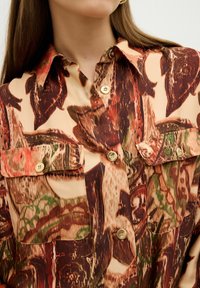 Bedruckte Bluse in erdigen Farbtönen mit großen Blattmustern, Knopfleiste, kurzen Taschen und Kragen. Glatte Textur.
