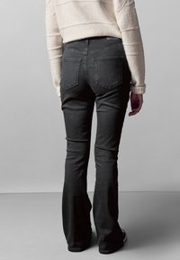 Jeans negros de campana con una cintura de altura media, bolsillos traseros y una textura de denim suave, combinados con una blusa de punto de color claro.