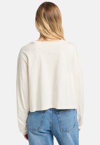 Cropped, long-sleeve shirt in light cream fabric with a relaxed fit. Smooth texture, wide neckline, and dropped shoulder seams.
