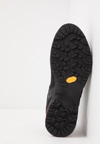 Černá podrážka turistické obuvi s drsným vzorkem, oranžovými akcenty, logem Vibram®, strukturovaným povrchem a pevnými vzory pro lepší trakci.