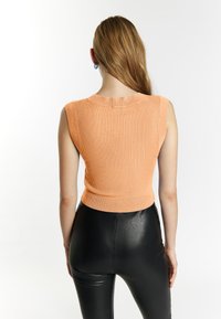 Ærmeløs, ribbet cropped top i blød orange strik med rund halsudskæring, parret med shiny sorte tætsiddende bukser.