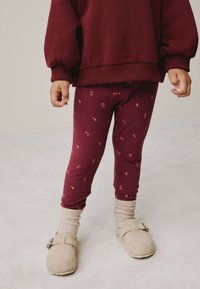 Bordó legice z majhnimi rumenimi in rdečimi cvetličnimi vzorci, kombinirane s prijetno bordó jopa in bež obutvijo.