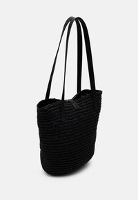 Mustavärinen kudottu olkalaukku, jossa on pitkät litteät hihnat, avoin yläosa ja teksturoitu pinta. Erityisen kevyt ja minimalistinen muotoilu.