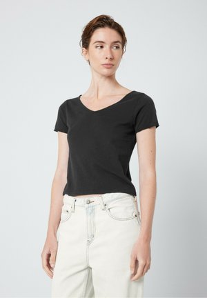 T-shirt noir à manches courtes en coton, coupe ajustée, longueur courte, texture lisse. Associé à un jean en denim clair taille haute.