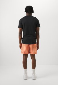 Camiseta negra de manga corta combinada con pantalones cortos a rayas naranjas. Hechos de algodón, los pantalones cortos presentan rayas verticales y una cinturilla elástica.