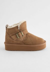 Stivale alla caviglia in suede marrone con fodera in pelliccia sintetica, suola piatta in gomma e una cinghia decorativa con fibbia sulla parte anteriore. Punta arrotondata.