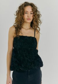 Top floreale nero realizzato in tessuto testurizzato con motivi di rose 3D. Presenta spalline sottili e una vestibilità ampia e stratificata.