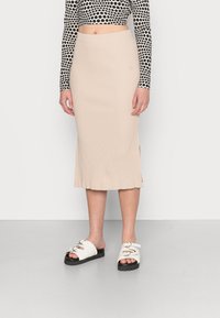 Beige, gerippter Midirock mit seitlichen Schlitzen, kombiniert mit weißen Slide-Sandalen mit einer klobigen schwarzen Sohle und dekorativen Hardware-Akzenten.