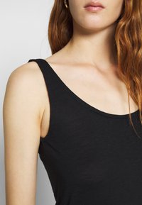 Černý bezrukávový top vyrobený z hladkého, lehkého materiálu, s širokým výstřihem a přiléhavým střihem.
