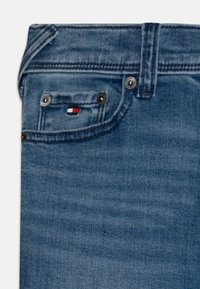 Niebieskie dżinsy o wyblakłym wykończeniu. Mają małą przednią kieszeń z czerwoną, białą i niebieską metką oraz widocznymi metalowymi elementami.