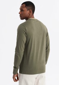 Olivgrünes Langarmshirt mit Rundhalsausschnitt, aus weichem Stoff, mit minimalen Nähten und einem entspannten Schnitt.
