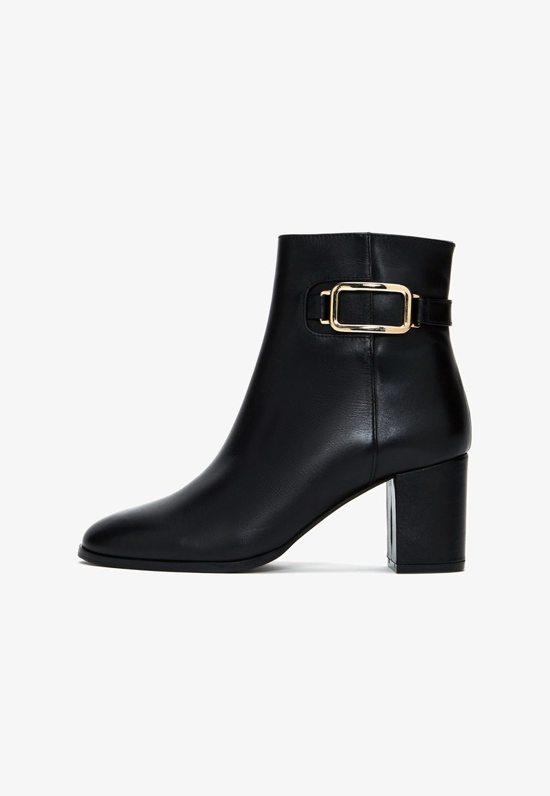 Botte de cheville en cuir noir avec un bout carré, un talon bloc de hauteur moyenne et un accent de boucle dorée sur le côté extérieur. Texture lisse.