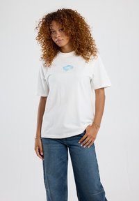 White cotton t-shirt with a relaxed fit, short sleeves, featuring a blue graphic design on the chest against a plain background.