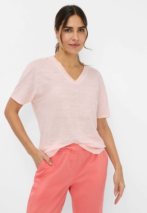 T-shirt rosa chiaro con scollo a V, realizzata in un tessuto morbido e texturizzato, con maniche corte, indossata con pantaloni corallo larghi.