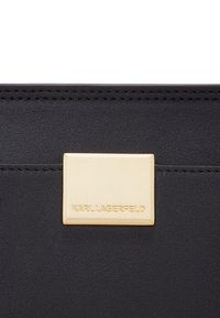 Portafoglio in pelle nera con una placca logo rettangolare dorata con "KARL LAGERFELD" inciso. Design elegante con cuciture in vista.