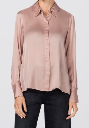 Satin long-sleeve blouse in soft pink with a collared neckline, front button closure, and gathered cuffs, paired with dark denim jeans.