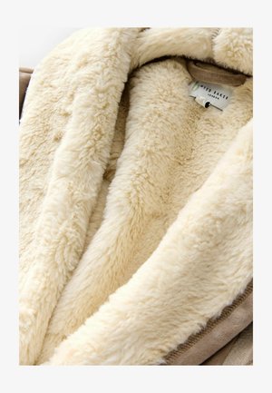 Beżowy materiał z sztucznego futra o miękkiej, puszystej teksturze, z kremowym, wewnętrznym podszewką. Zawiera metkę z napisem "Wild Baker London."