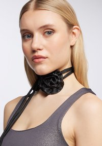Chocker in satin nero con design a rosa adornato con piccole perline; presenta due nastri regolabili e si abbina a un top grigio senza maniche.