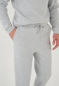 Conjunto de sudadera y pantalones de chándal gris, fabricado con tejido texturizado. Cuenta con una cintura con cordón y bolsillos laterales. Puños acanalados en las mangas.