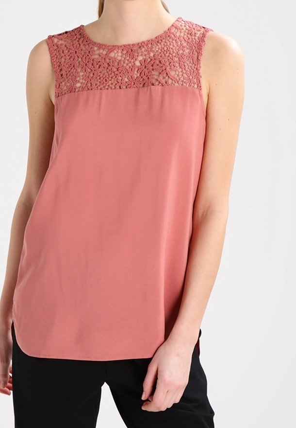 Haut sans manches couleur pêche avec un empiècement en dentelle et un tissu lisse, doté d'un col arrondi et d'une coupe décontractée, associé à un pantalon foncé.