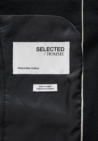 Un tissu noir avec une texture lisse présente deux étiquettes : l'une indique "SELECTED / HOMME" et "Responsably Crafted", l'autre "FABRIQUÉ EN TURQUIE".