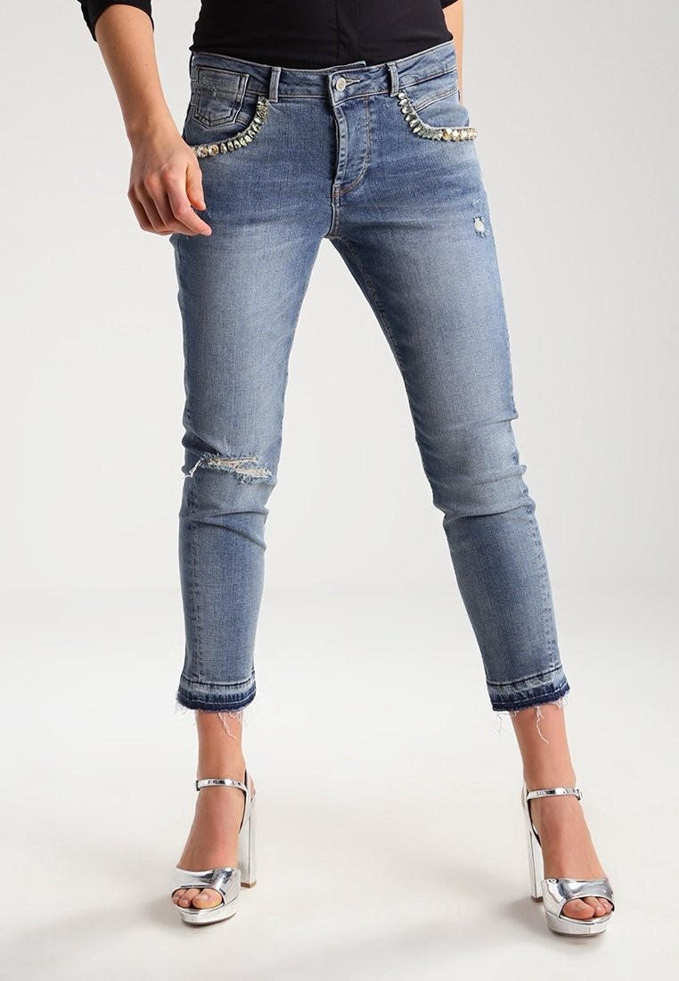 Smal ljusblå denimjeans med ett slitna mönster, dekorerade fickor och fransad nederkant. Matchas med silverfärgade högklackade sandaler.